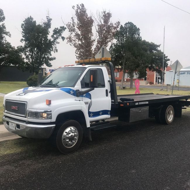 White GMC tow truck on a street, with an empty flatbed.