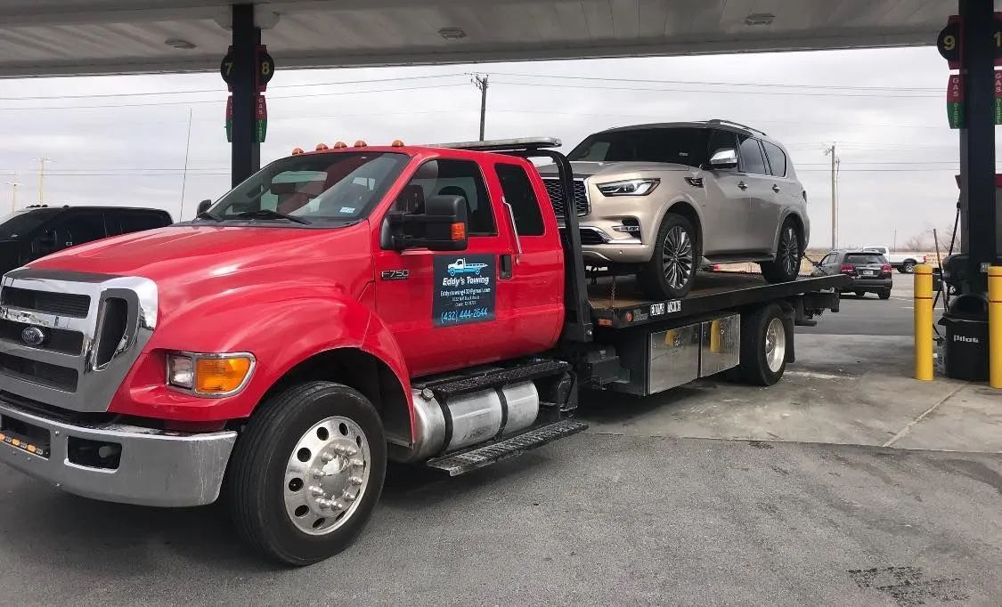 Red tow truck hauling a silver SUV at a gas station.