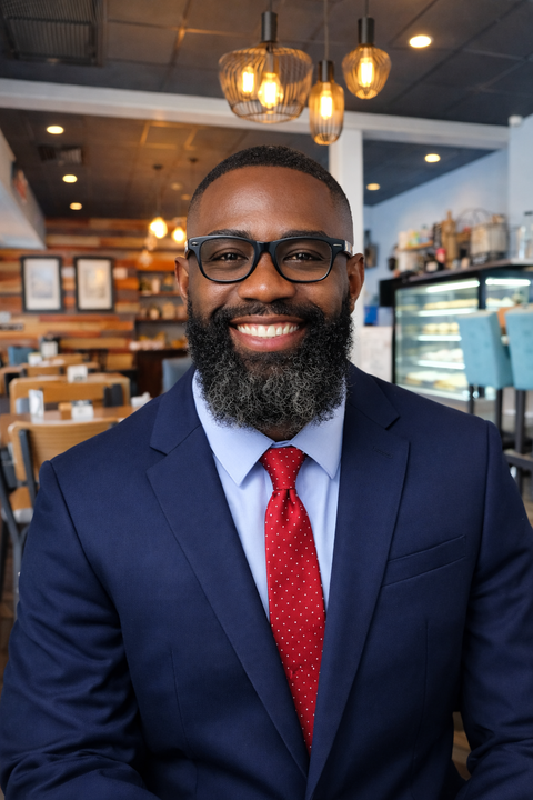 Smiling man in a navy suit and red tie inside a warmly lit café