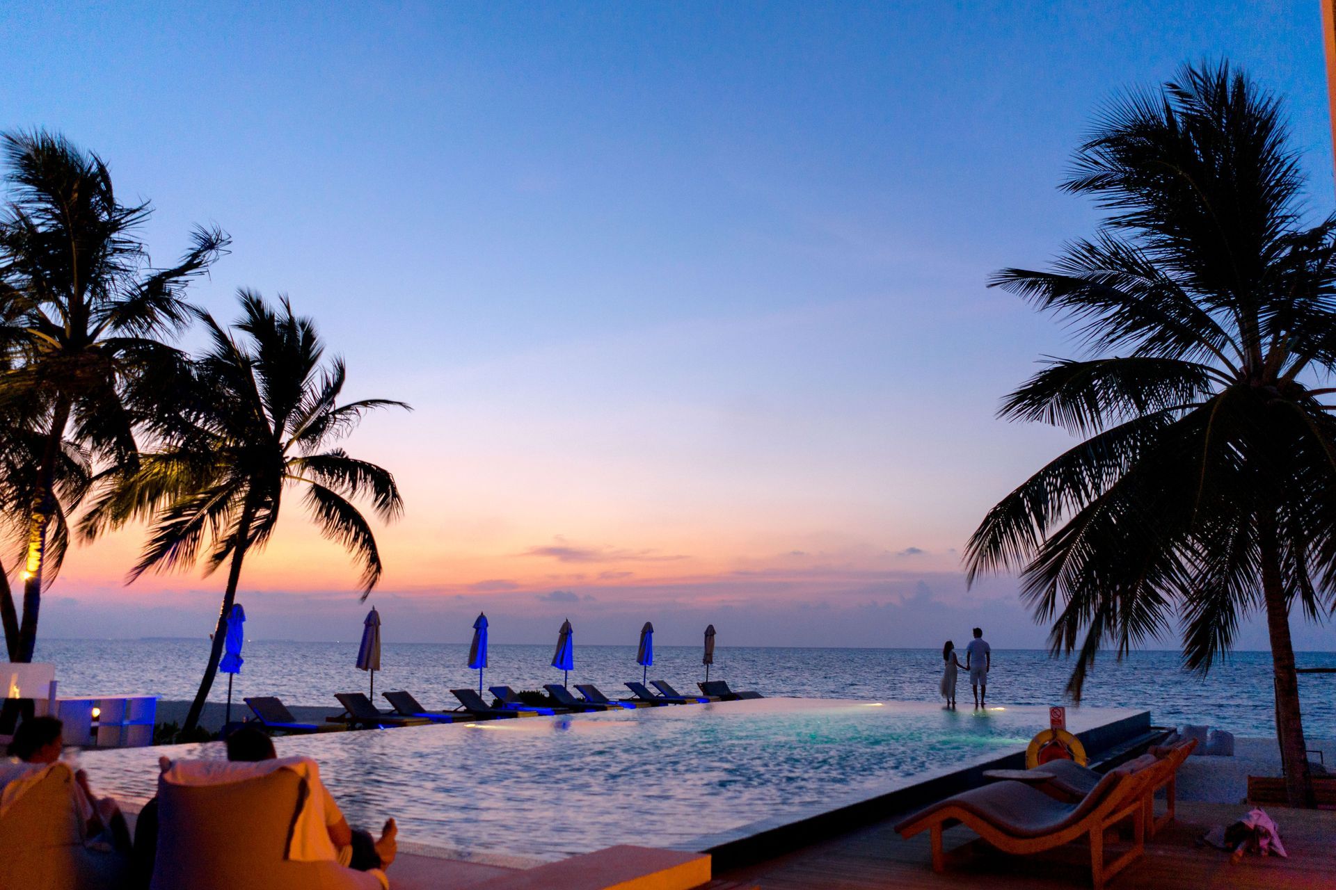 Sunset beach resort with palm trees, lounge chairs, and people by the ocean