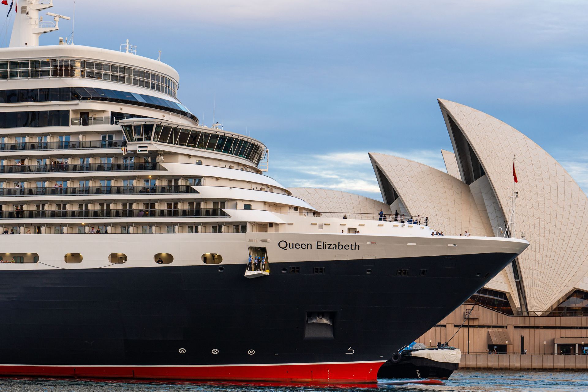 Large cruise ship docked near the Sydney Opera House under a blue sky