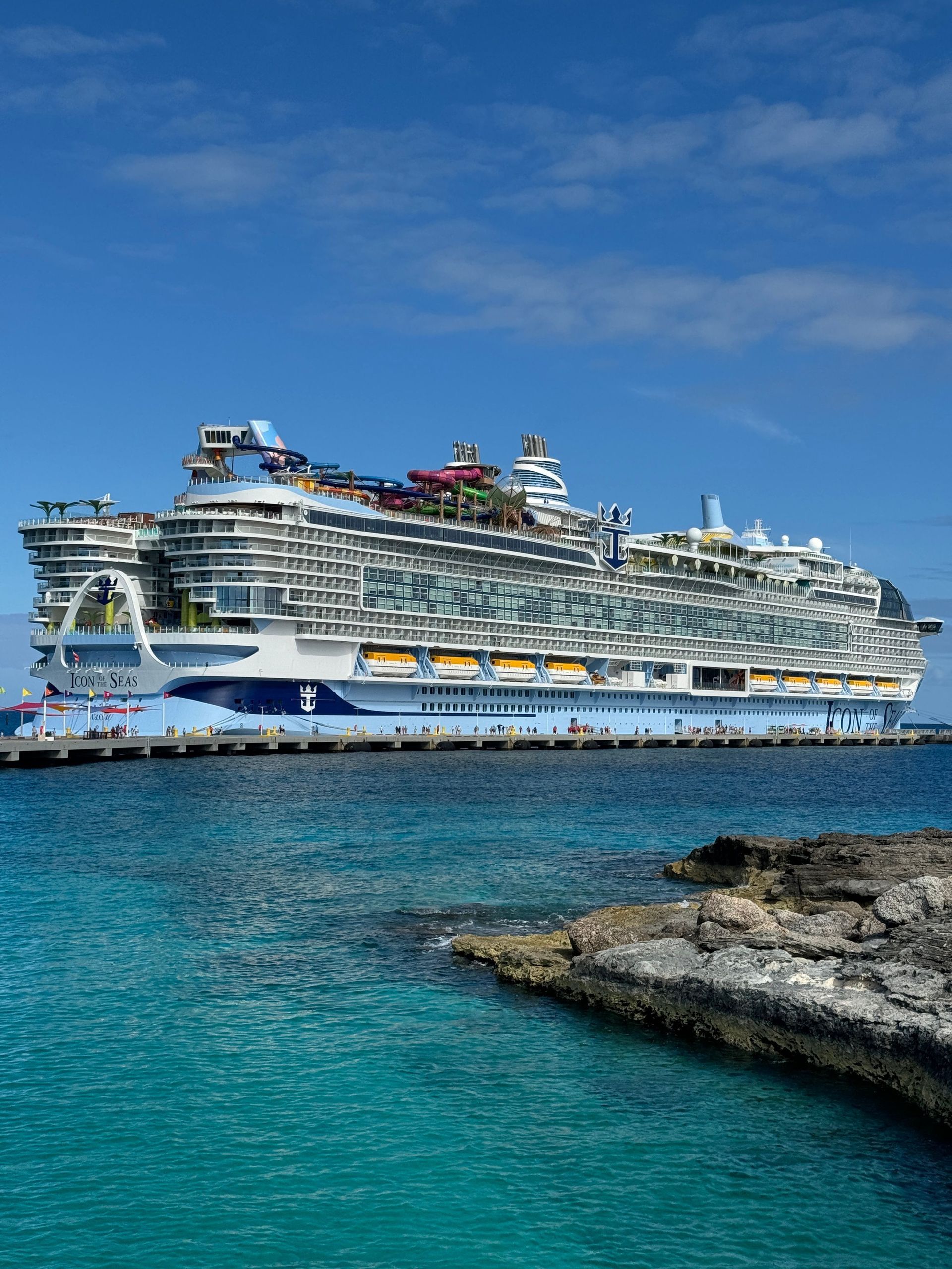 Large white cruise ship in turquoise water near a rocky shore under a clear blue sky