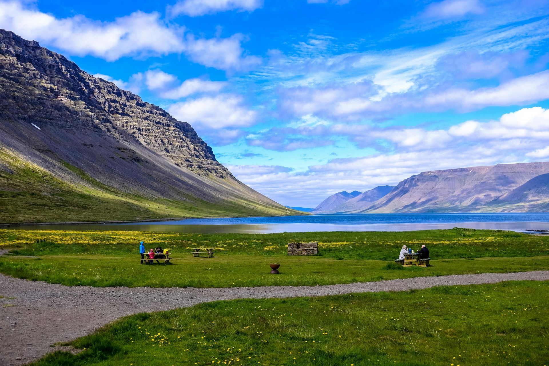 Mountain lake valley with green meadow, rocky slopes, and a bright blue sky with clouds.