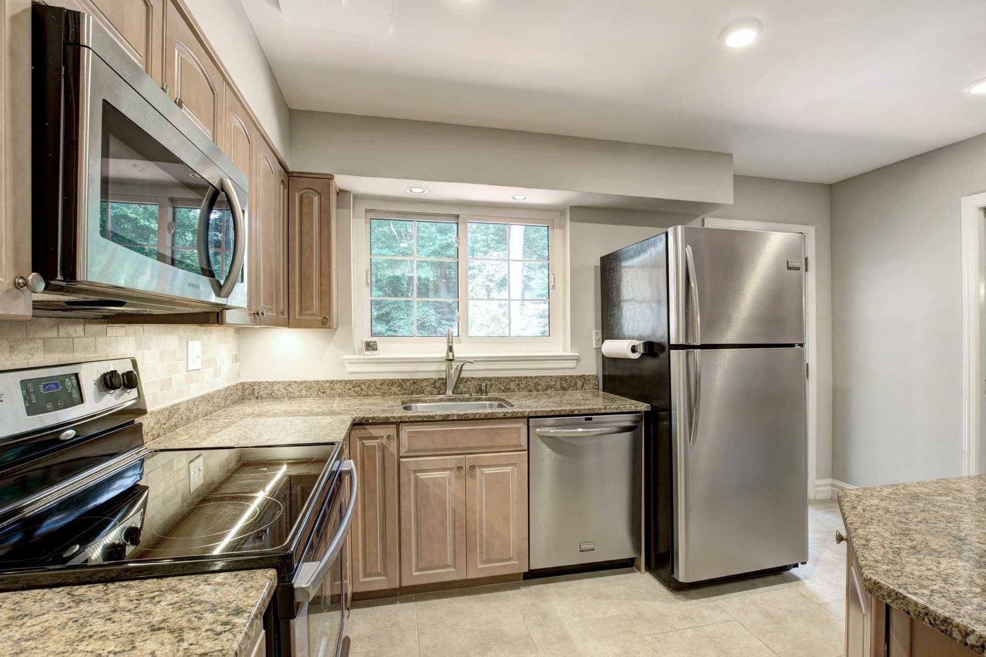 Modern kitchen with stainless steel appliances, granite counters, and a window over the sink