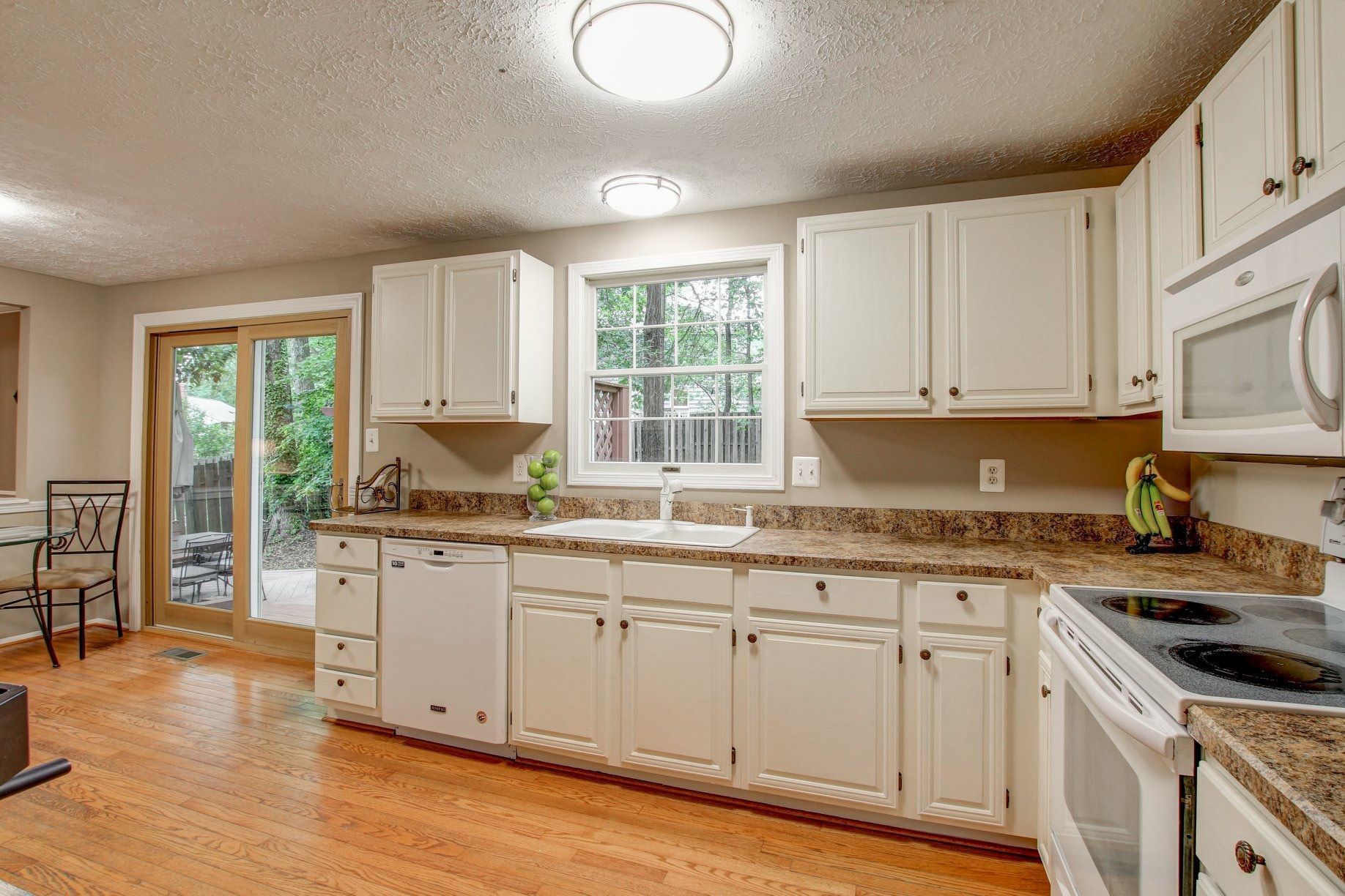 Bright kitchen with white cabinets, granite counters, hardwood floors, and a sliding glass door to a deck