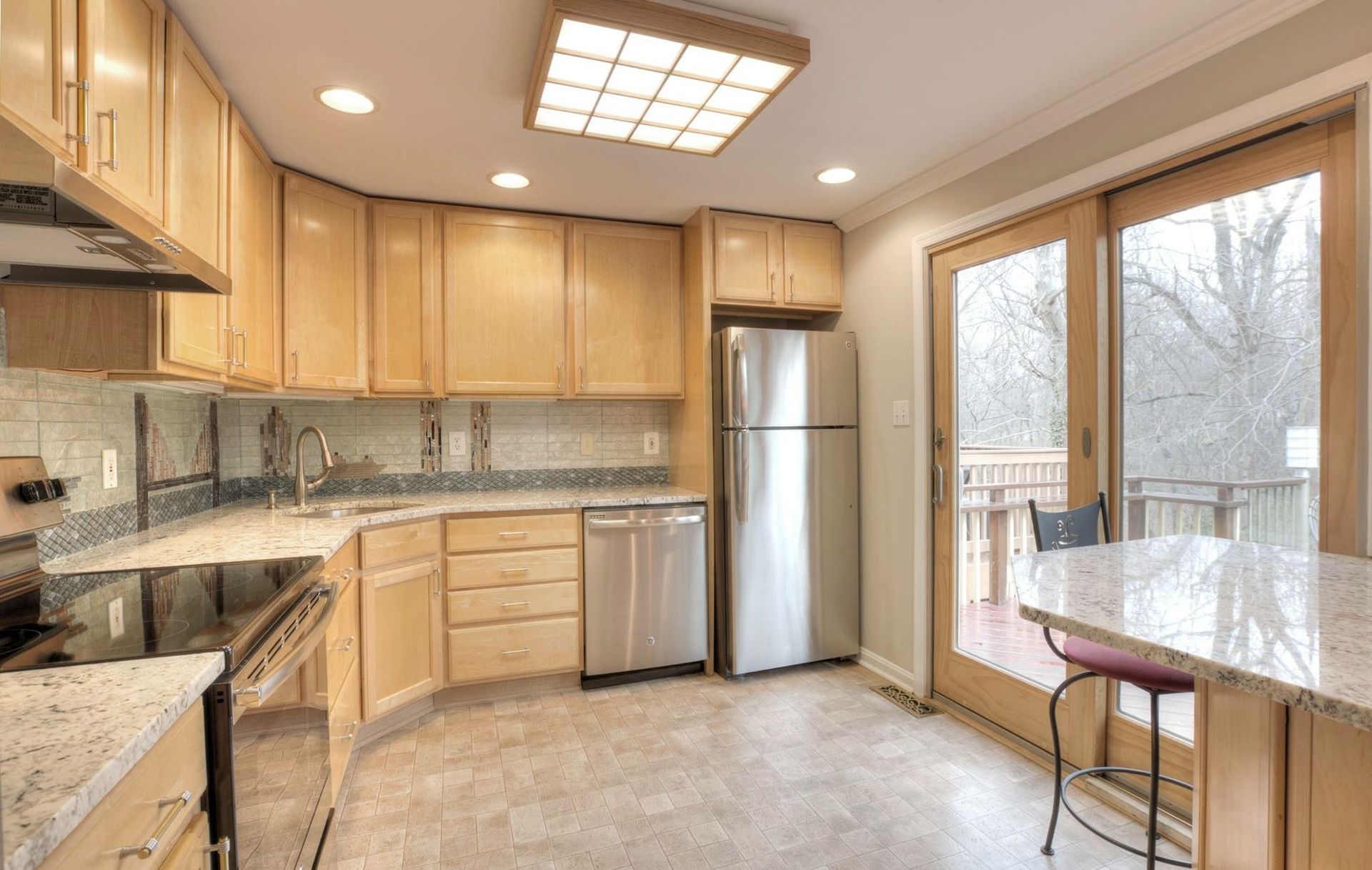 Bright kitchen with light wood cabinets, granite counters, stainless fridge, and a windowed breakfast nook.