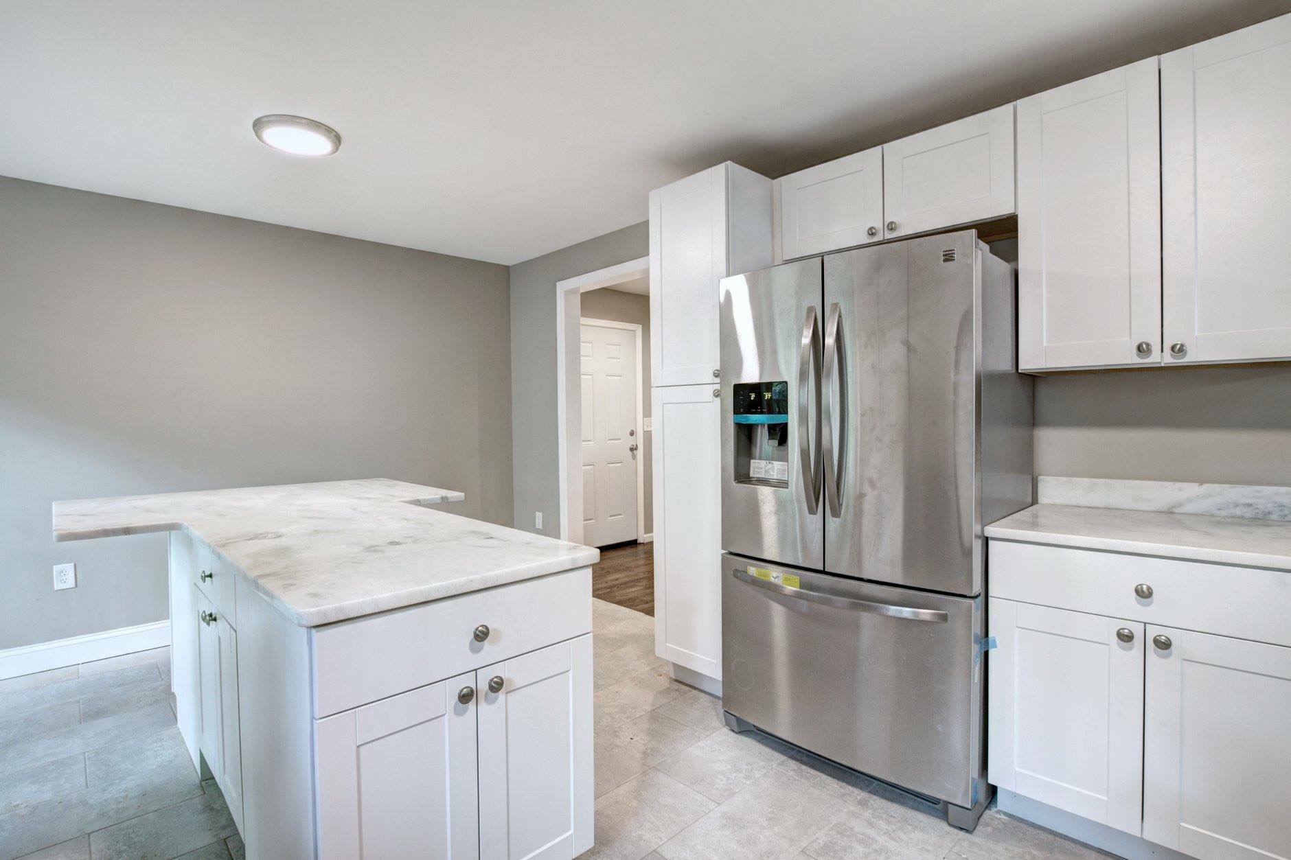Bright white kitchen with stainless steel fridge, island, and cabinetry under recessed ceiling lights