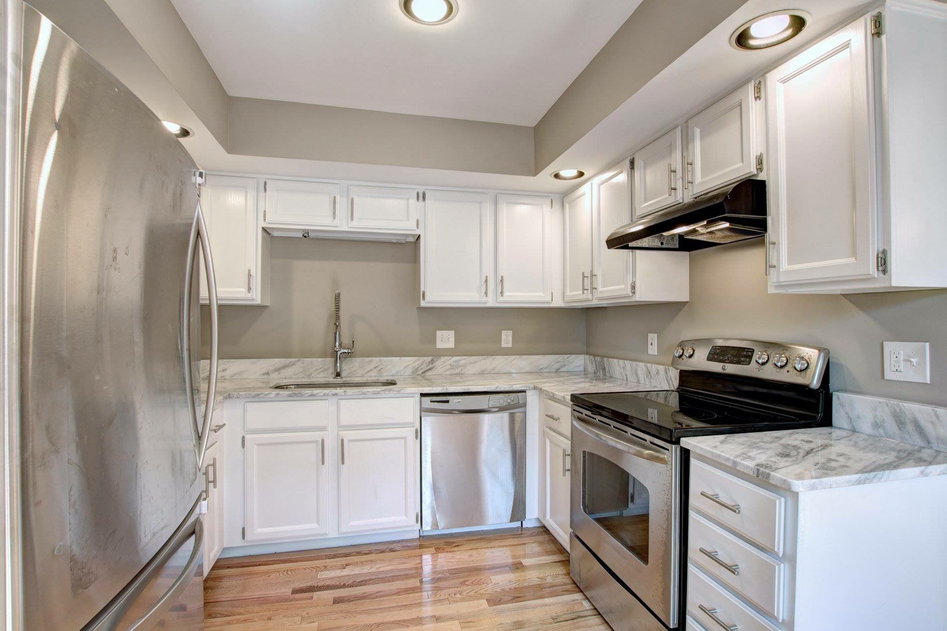 Bright modern kitchen with white cabinets, stainless appliances, marble counters, and hardwood floors