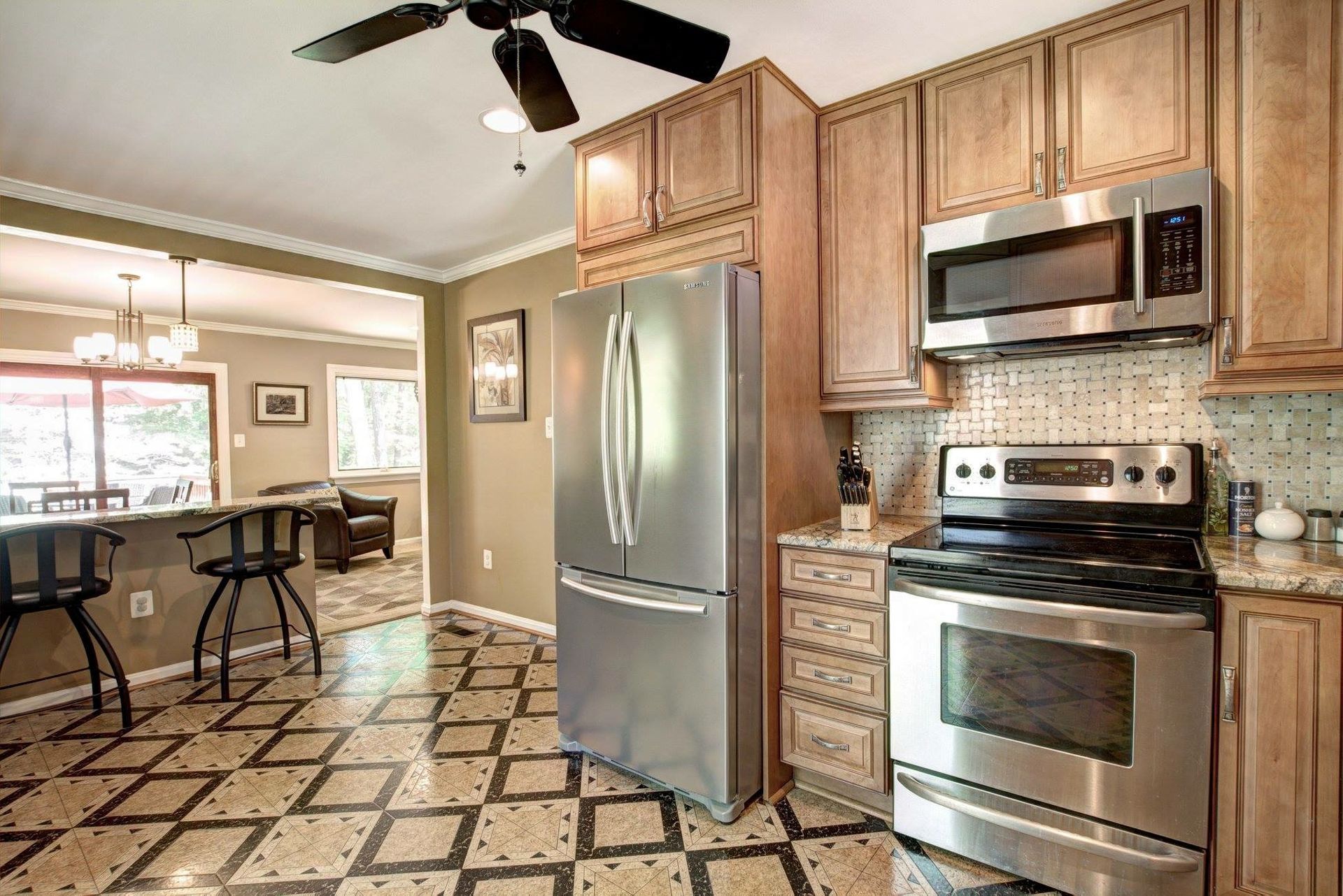 Bright kitchen with stainless steel appliances, patterned floor, and adjacent dining area with bar stools.