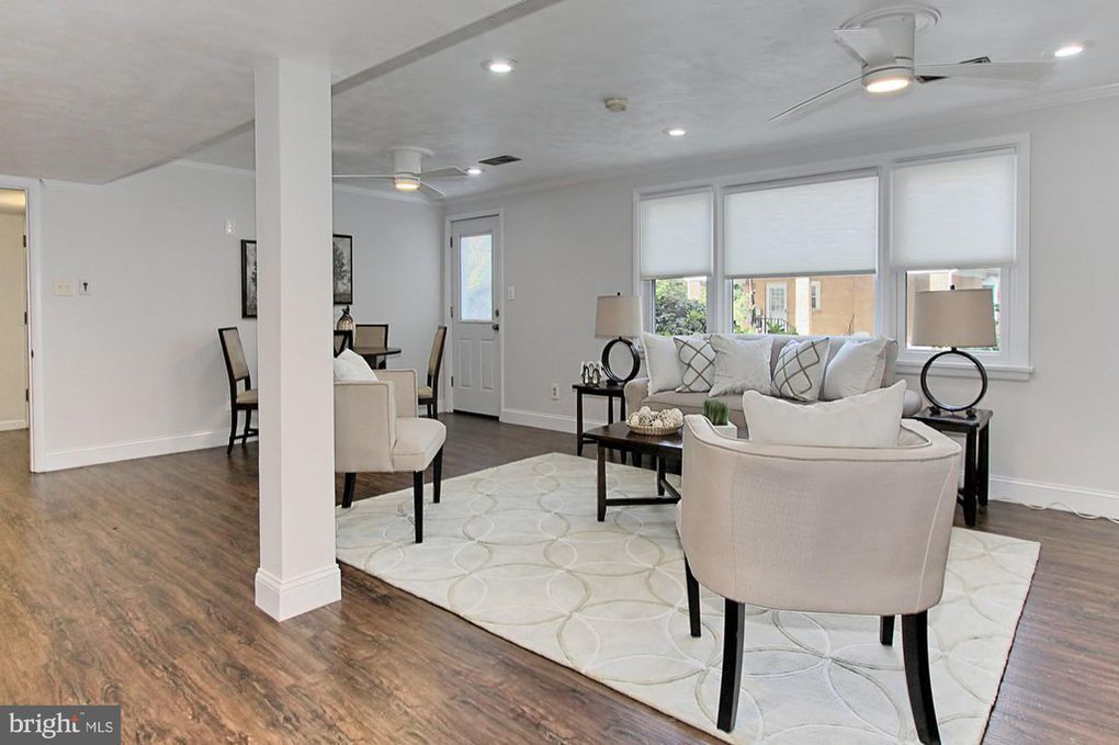 Bright living room with white chairs, black tables, large windows, and wood floors