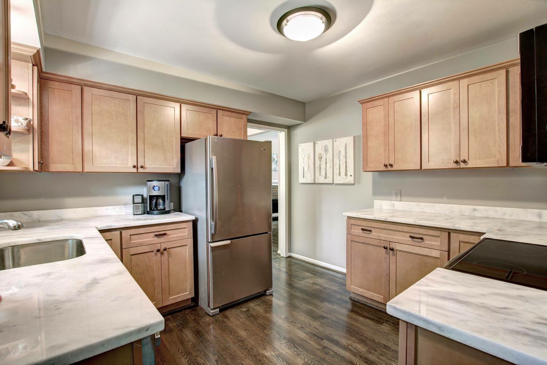 Bright kitchen with light wood cabinets, stainless fridge, white counters, and dark wood floors.