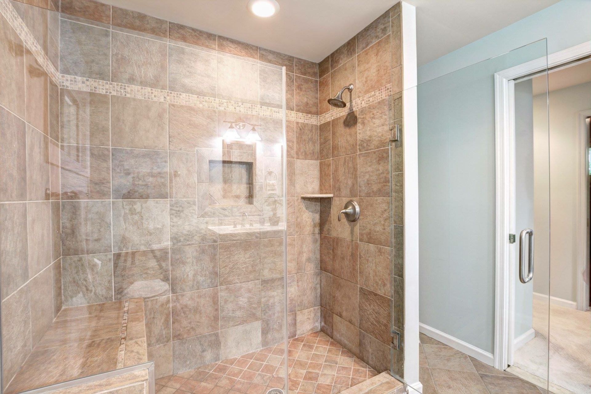 Modern tiled walk-in shower with glass enclosure and adjacent bathroom vanity area