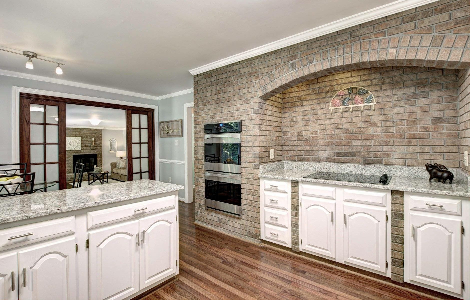Modern kitchen with white cabinets, marble countertops, wood floors, and a brick arch alcove