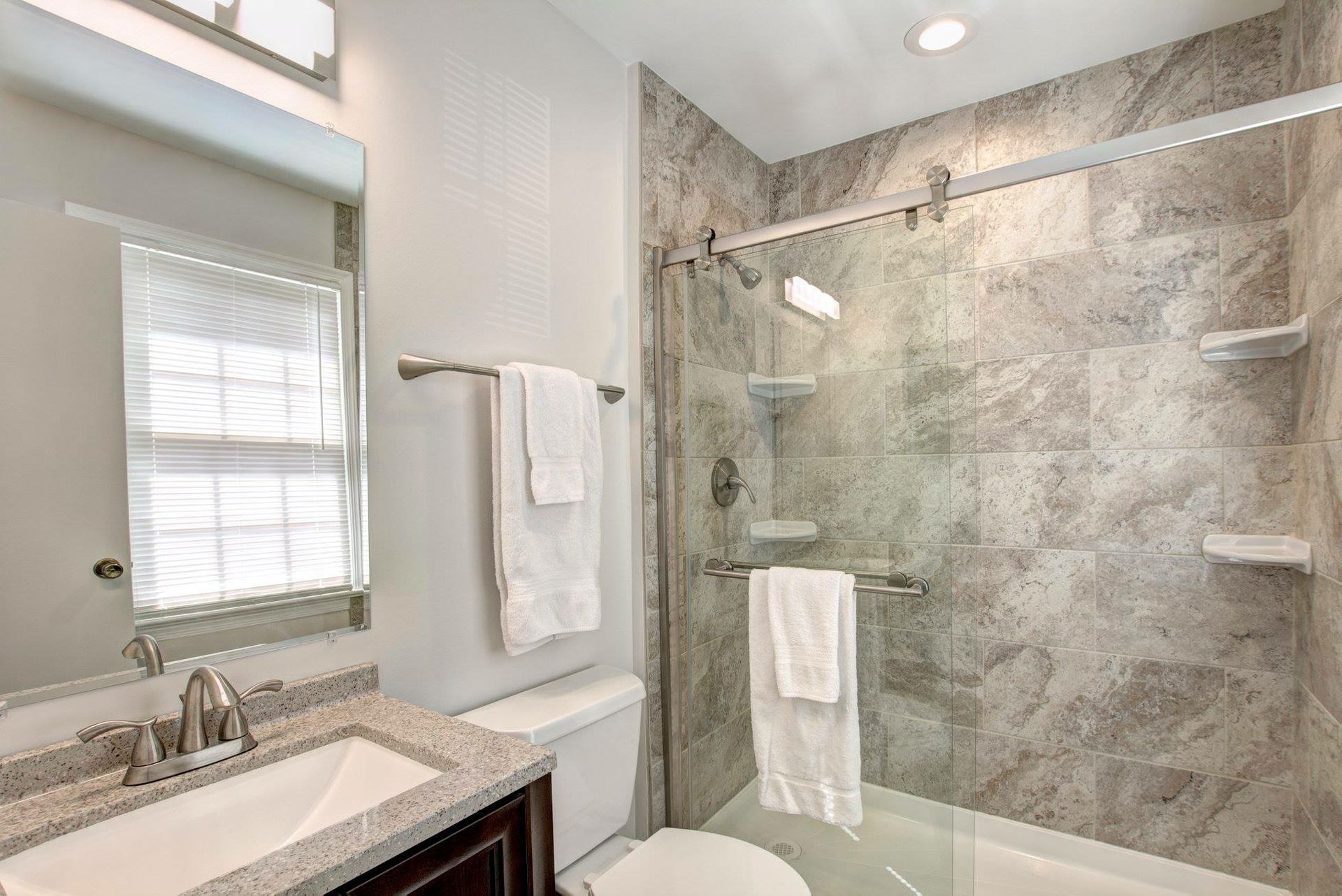 Small bathroom with a glass shower, marble tile, vanity sink, and wall mirror.