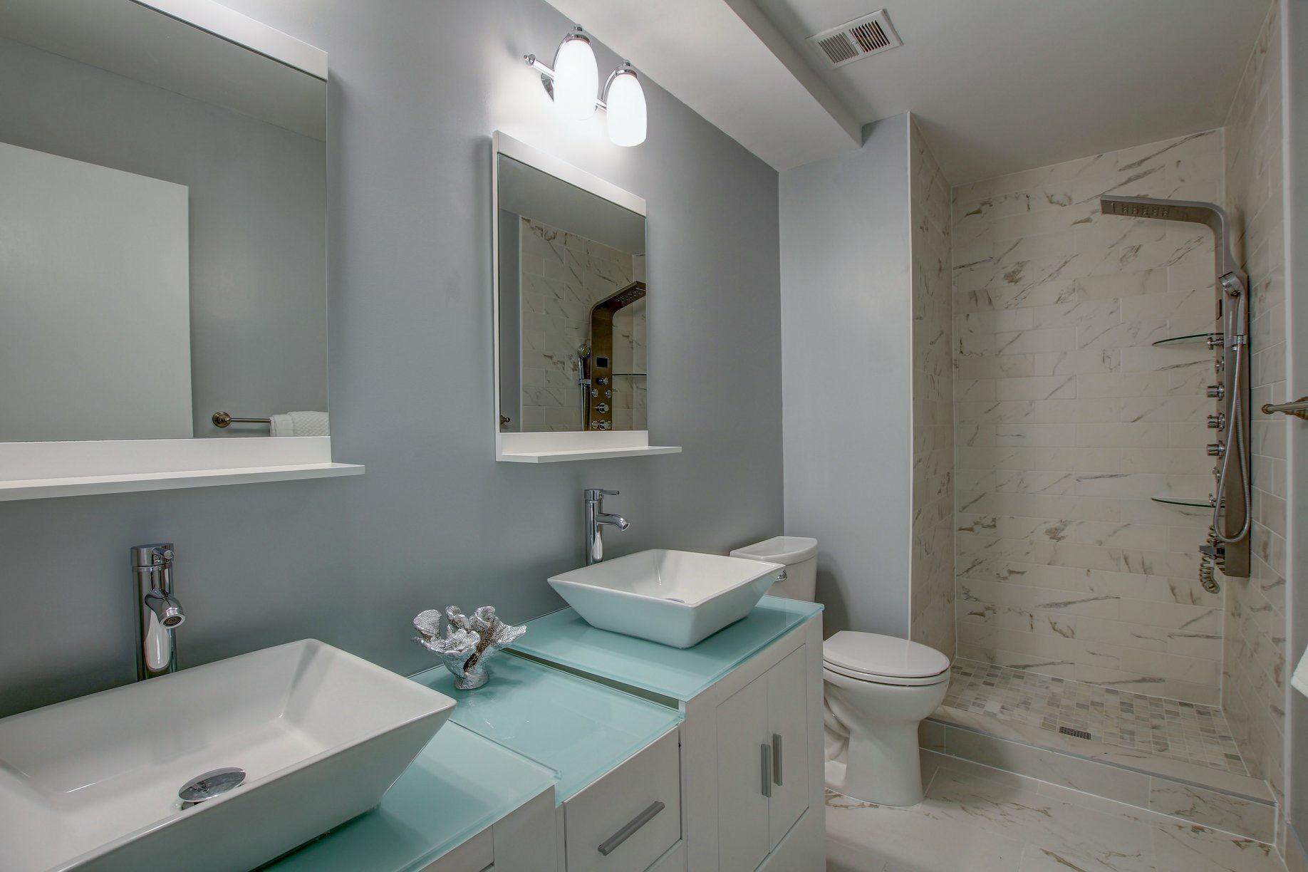 Modern bathroom with dual sinks, mirrors, toilet, and marble-tiled shower