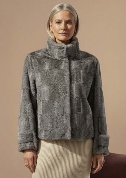 Frau in einer grauen Kunstpelzjacke mit hohem Kragen und Manschettenärmeln über einem cremefarbenen Rock.