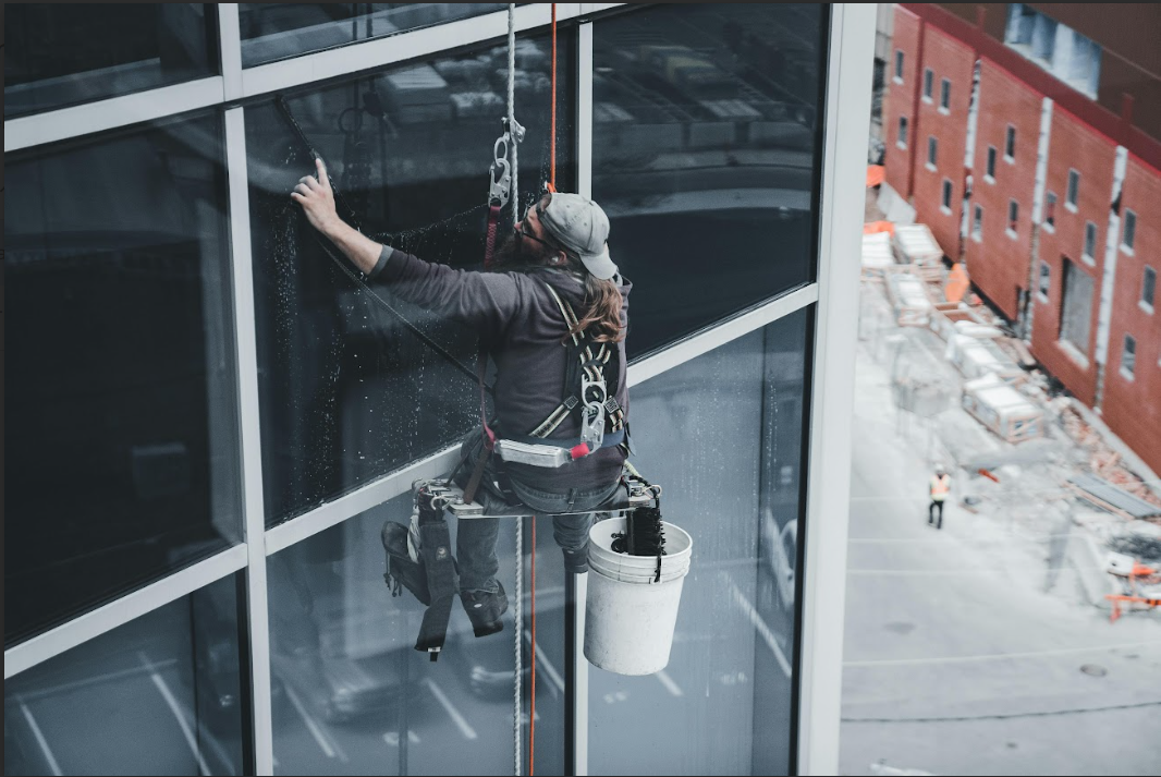 A man is cleaning the windows of a building from a rope.