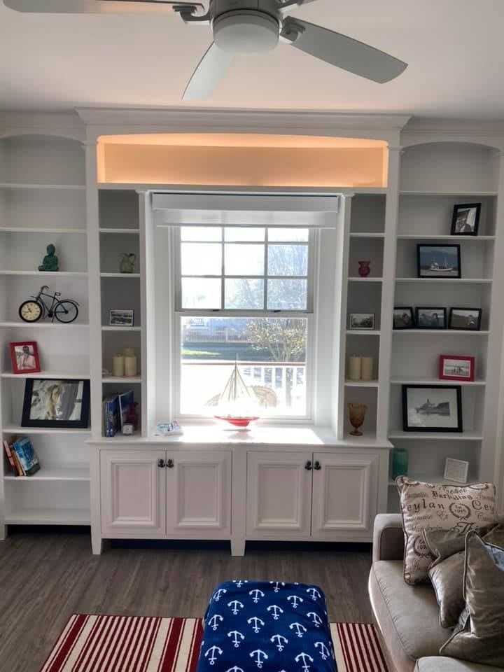 a living room with custom built-ins behind a ceiling fan and a window