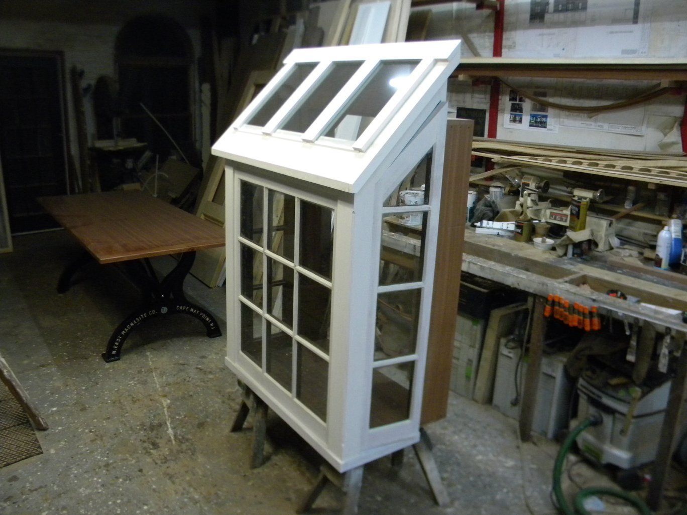 a custom built white window with a roof is sitting on a table in a workshop