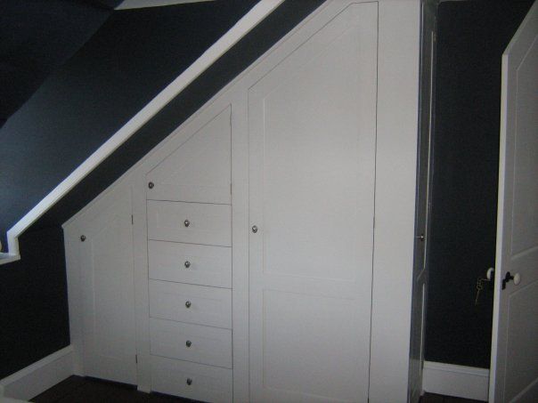 a custom built closet under a staircase with drawers and doors