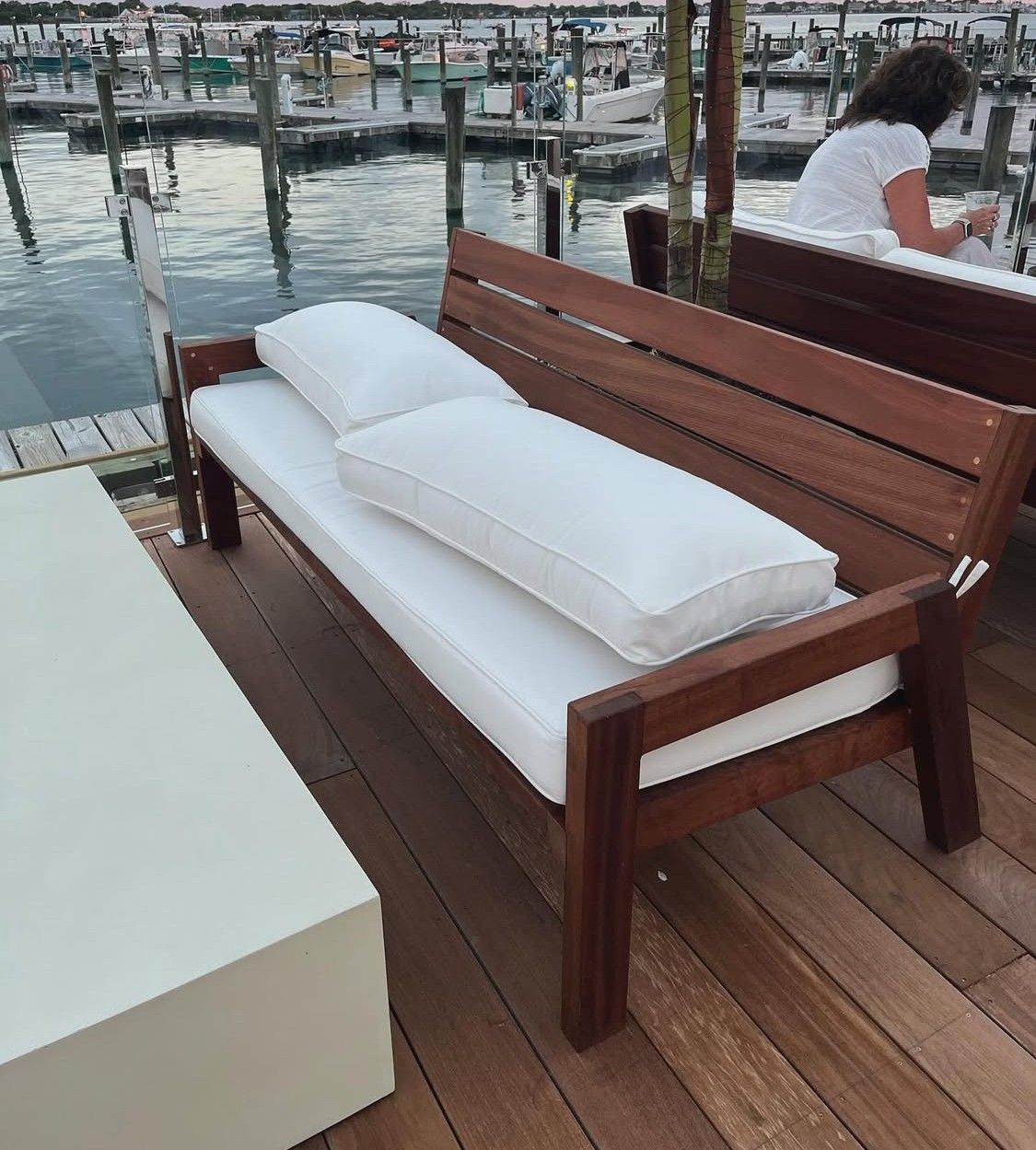 A wooden bench with white cushions sits on a wooden deck