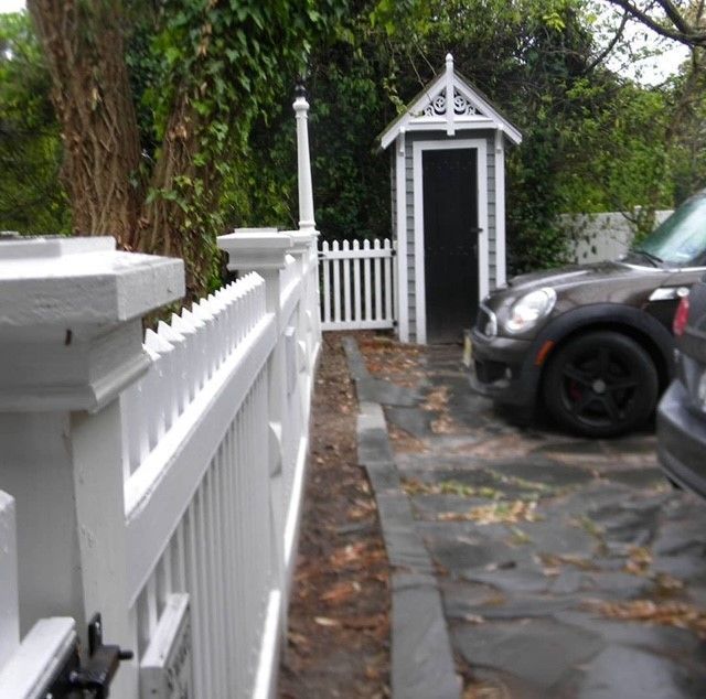 a car is parked next to a white picket fence with a small custom built guard house
