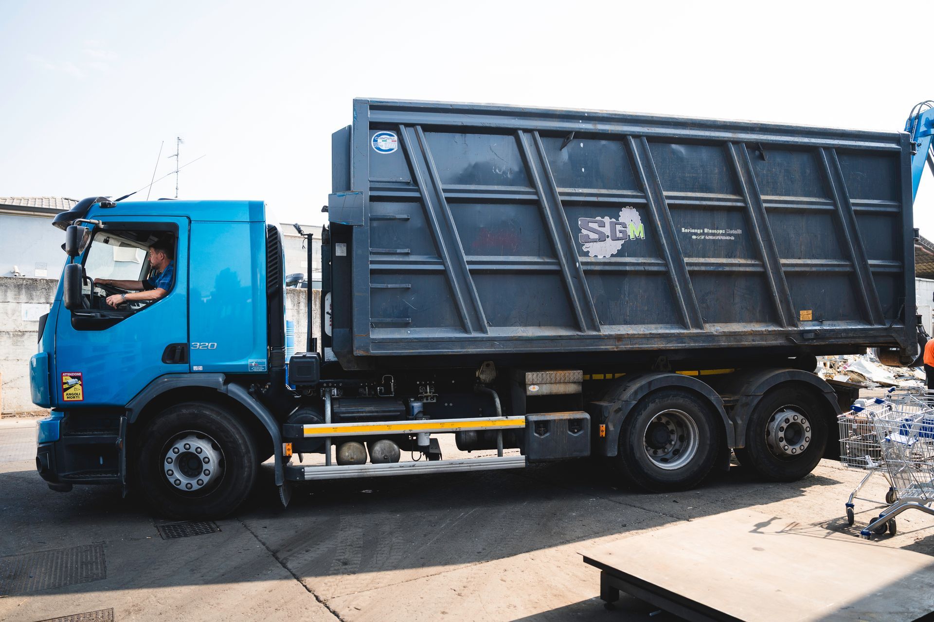 Camion della spazzatura verde con cabina blu parcheggiato accanto a un edificio in una strada