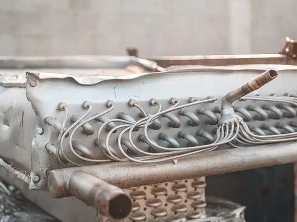 Primo piano di un serbatoio metallico con fili avvolti, valvole e un tubo flessibile intrecciato.