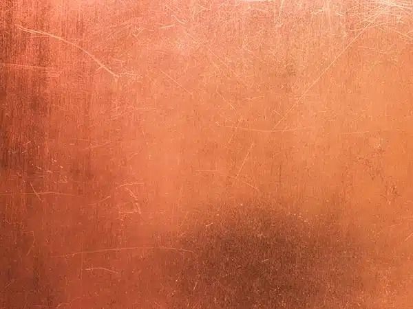 Superficie ruvida di colore arancio-marrone con lievi graffi e sfumature più scure vicino al centro.