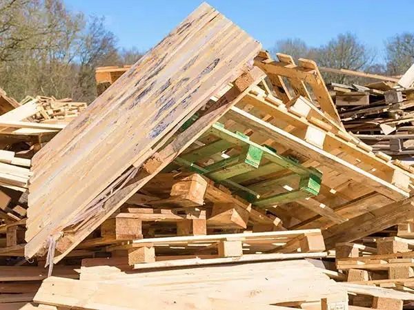 Una pila crollata di pallet e legname all'aperto, sotto un cielo azzurro.