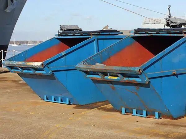 Cassonetti industriali blu e arancioni allineati su un molo in riva al mare