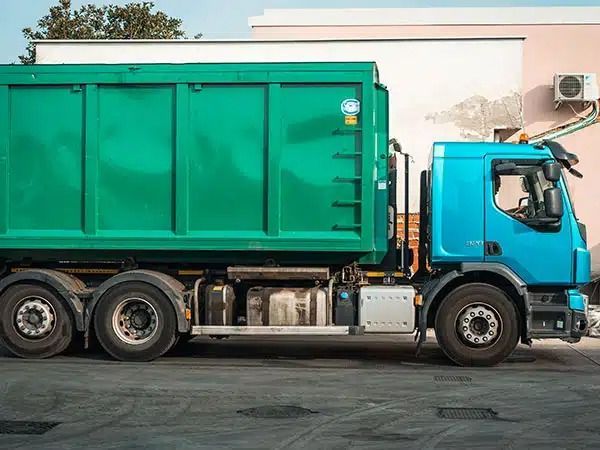 Camion della spazzatura verde con cabina blu parcheggiato accanto a un edificio in una strada