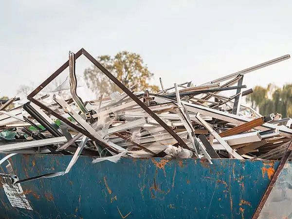 Un cassonetto blu stracolmo di travi di legno rotte e rottami metallici all'aperto.