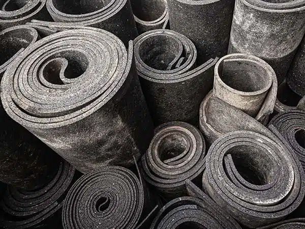 Pile di tappeti o stuoie grigie arrotolate e accatastate una accanto all'altra in un'area di stoccaggio.