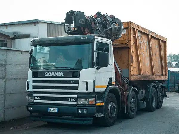 Autocarro ribaltabile Scania bianco carico di rottami metallici parcheggiato accanto a un magazzino.