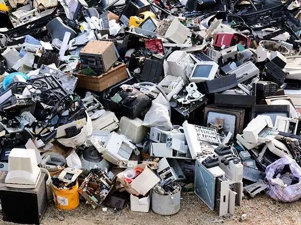 Cumulo di apparecchiature elettroniche e attrezzature per ufficio scartate in una discarica.