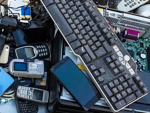 Un mucchio di vecchi apparecchi elettronici, tra cui tastiere e telefoni cellulari, sparsi in una scatola disordinata.