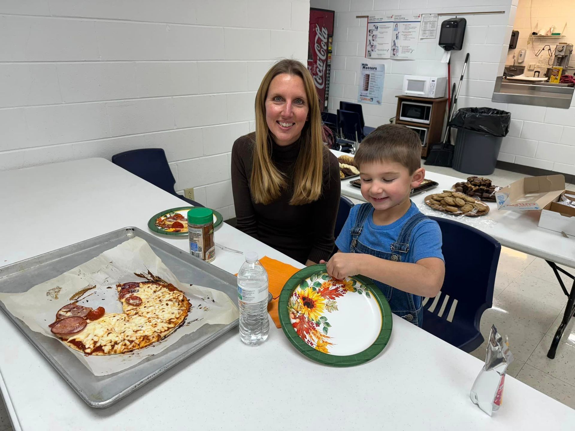 A woman and a child are sitting at a table with plates of food at a PTL meeting.