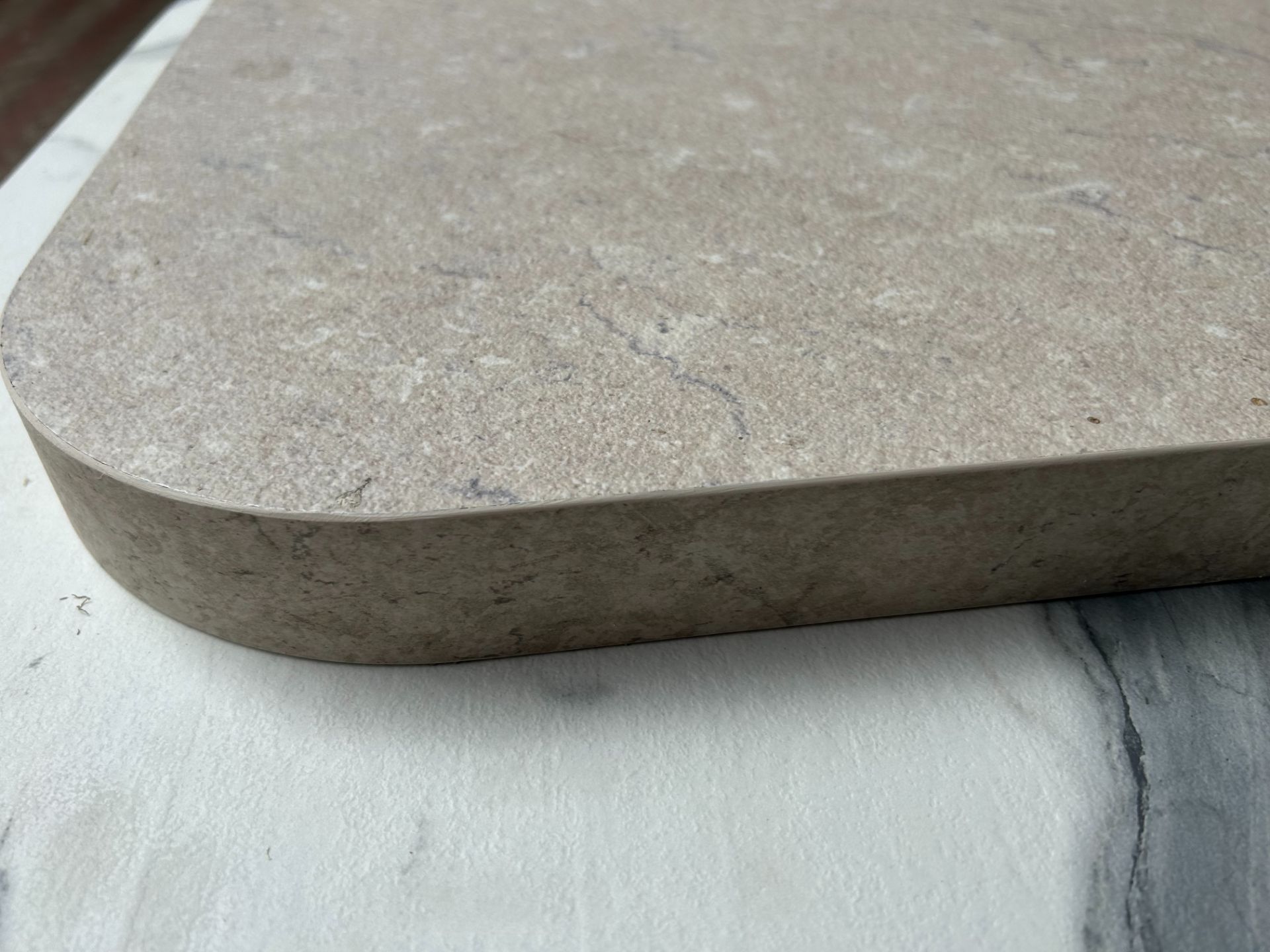 Primo piano di una lastra di pietra beige arrotondata appoggiata su una superficie bianca ruvida.