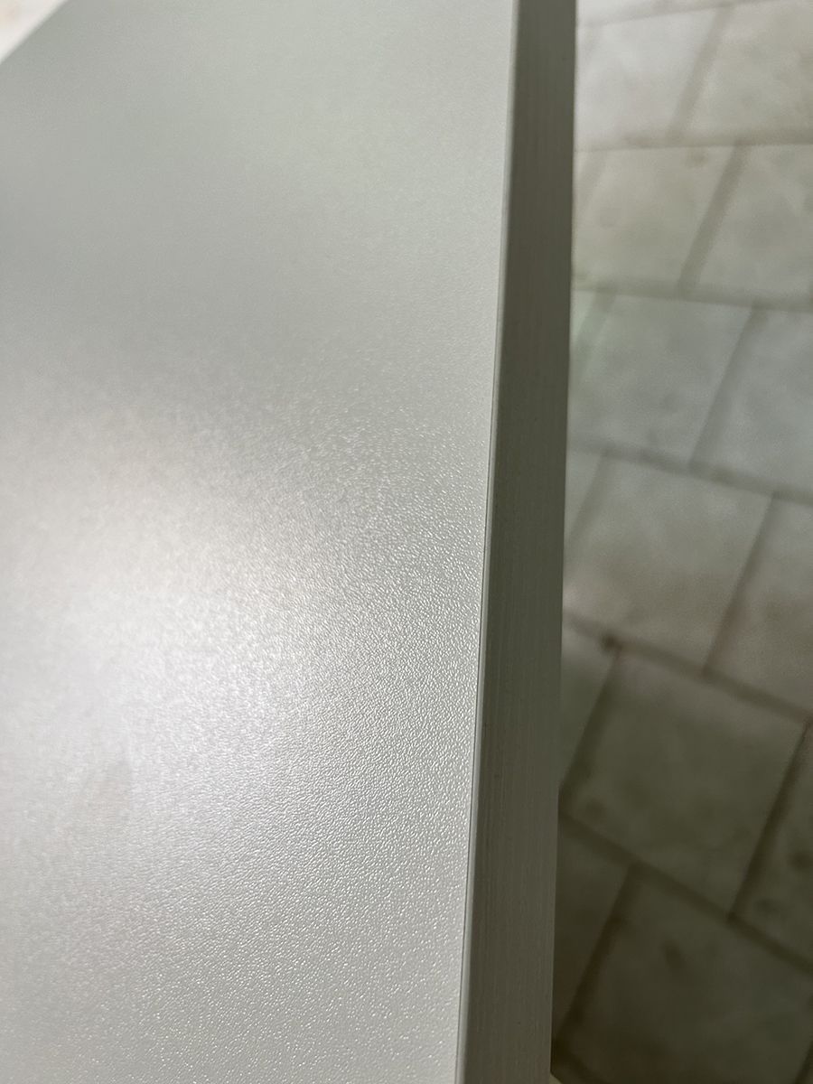 Primo piano di un angolo di parete grigio chiaro con superficie ruvida, accanto a piastrelle del pavimento beige.
