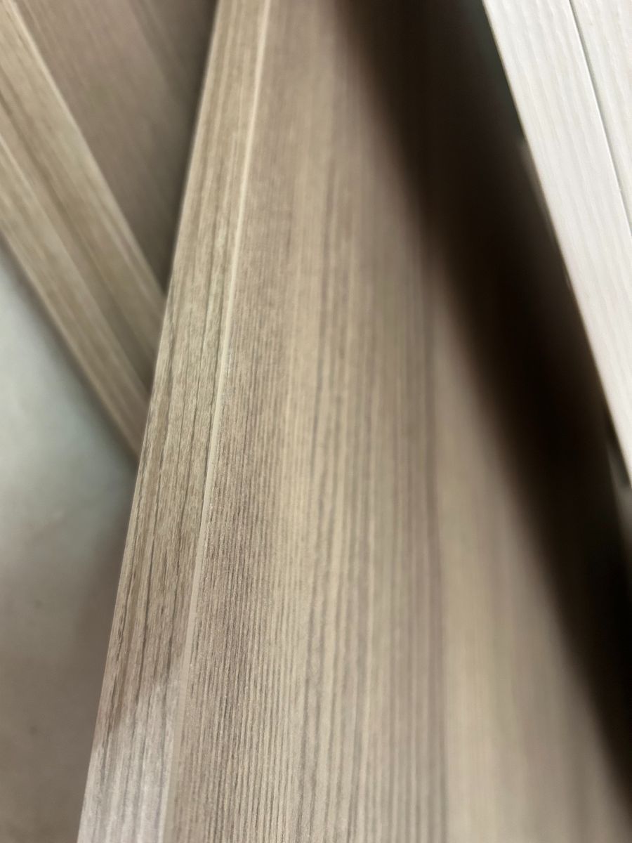 Primo piano di pannelli con venature di legno chiaro, ombre diagonali e uno stretto spazio tra le superfici.