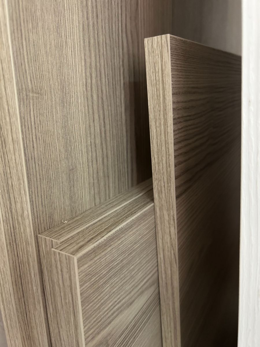 Le ante del mobile con finitura effetto legno sono leggermente socchiuse, lasciando intravedere una stretta fessura scura tra di esse.