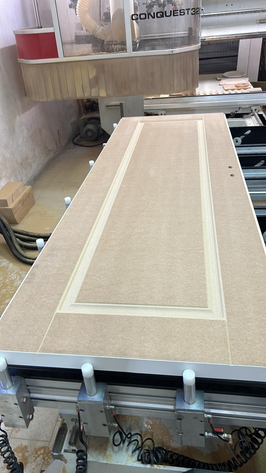 Pannello di un'anta di un armadio in legno, fissato con morsetti a un banco da lavoro in un'officina, con un bordo rettangolare incassato.