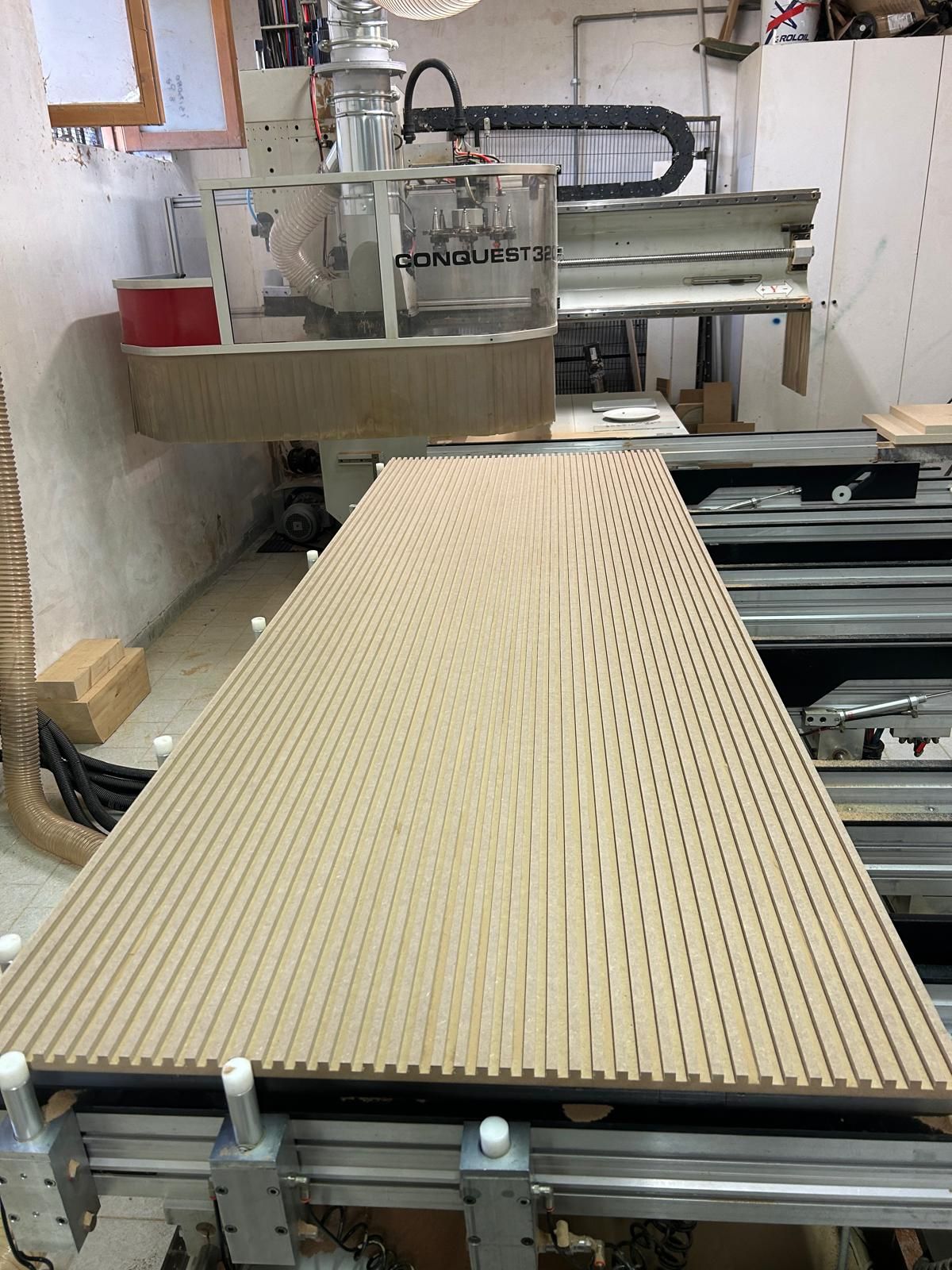 Una fresatrice CNC taglia un pannello di legno perforato su un banco da lavoro in un'officina.