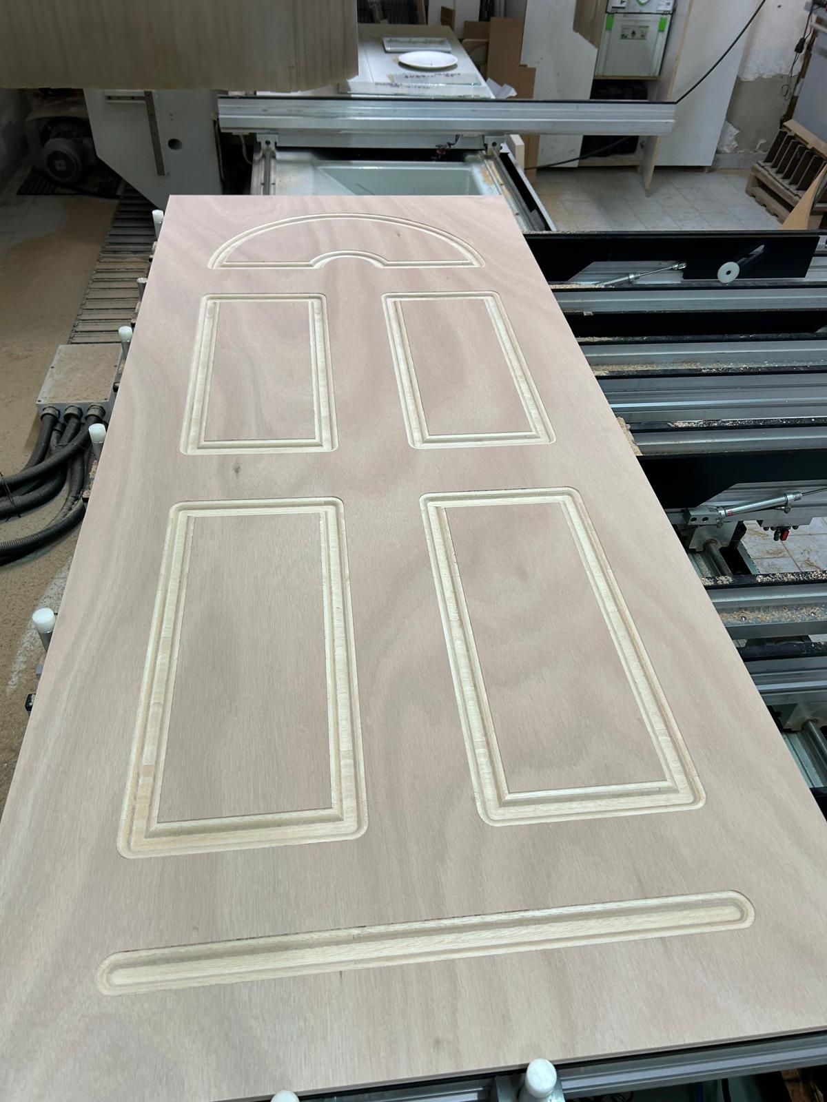 Pannello per porta in legno tagliato a CNC con contorni fresati su un banco da lavoro di una macchina officina.