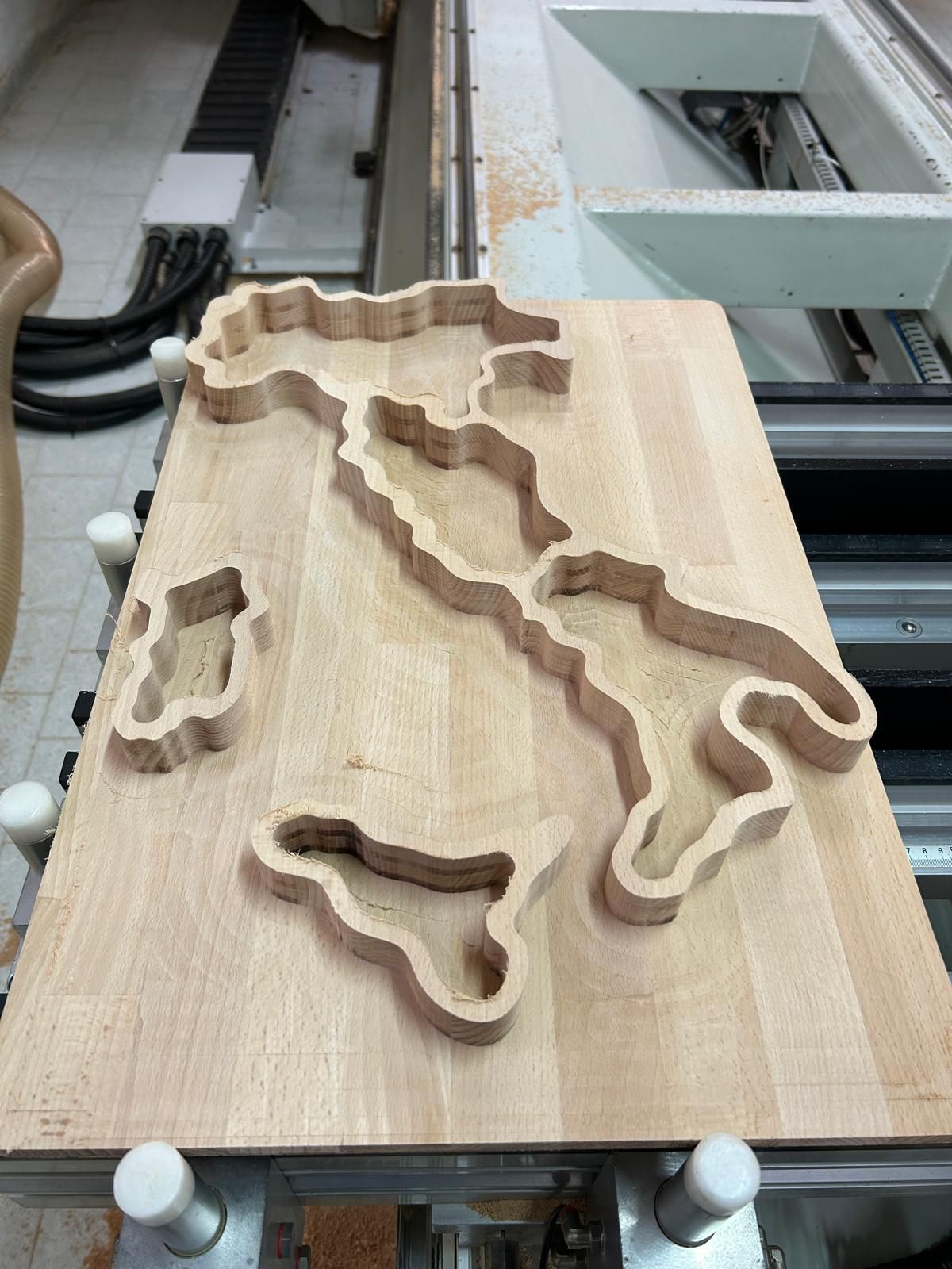 Sagome di legno a forma di mappa su un banco da lavoro in un'officina, tra cui una grande sagoma dell'Italia.