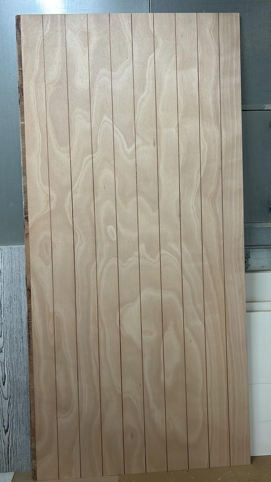 Pannello alto in legno chiaro con motivo a listelli intrecciati, appoggiato a una parete.
