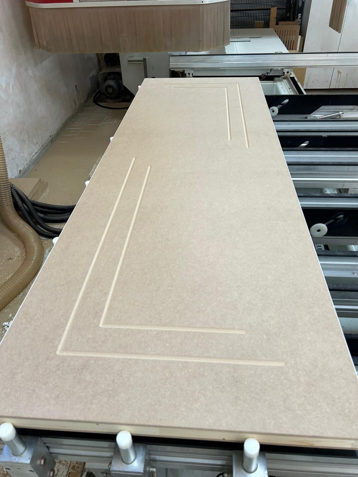 Ampio pannello rettangolare beige con scanalature a L fresate su un banco da lavoro per officina.