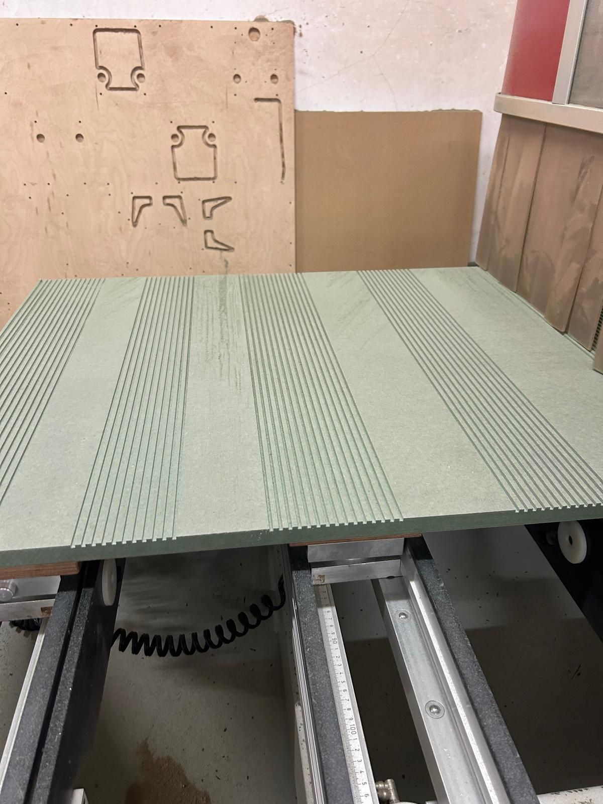 Tavolo verde forato in un'officina, con pannelli di legno e binari metallici visibili al di sotto.