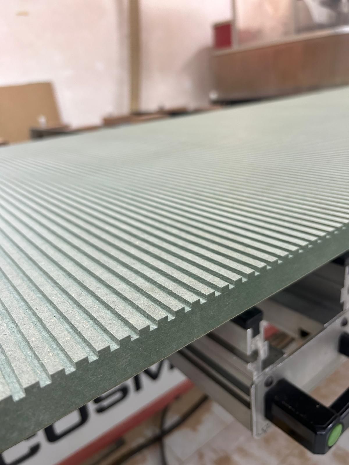 Primo piano di un pannello metallico verde scanalato su un macchinario in un ambiente industriale.